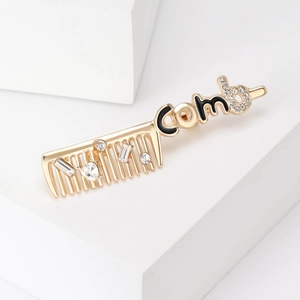 Close-up of golden comb brooch with inlaid rhinestones and comb lettering detail