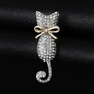 Detailed close-up of a silver cat brooch with white rhinestones and a gold bow tie