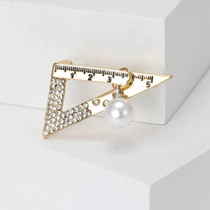 Macro detail of gold-toned triangle ruler brooch with rhinestones and pearl pendant