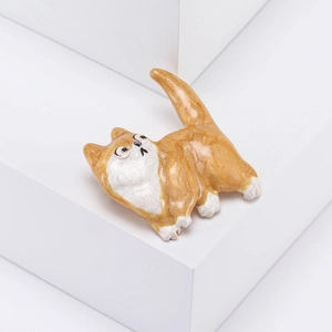 Macro d'une broche chat en émail orange et blanc sur un support géométrique blanc pur