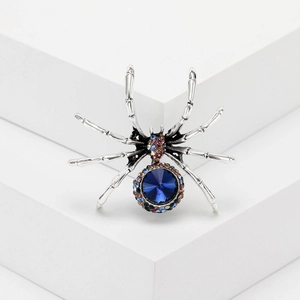 Vintage spider brooch with dark blue crystal and rhinestones on a white geometric block