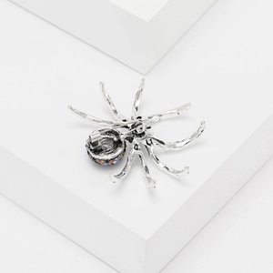 Macro shot of silver-tone spider brooch with colorful rhinestones on white platform