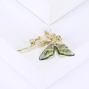 Detailed close-up of a golden fairy brooch with translucent green wings and pearl detail