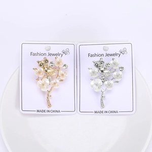 Close-up of owl brooches with white enamel flowers and rhinestones on jewelry cards