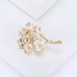 Detail view of owl and flower brooch with white petals and clear crystals on gold base