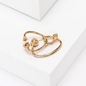 Macro detail of a golden stethoscope brooch with pin closure on a white stand