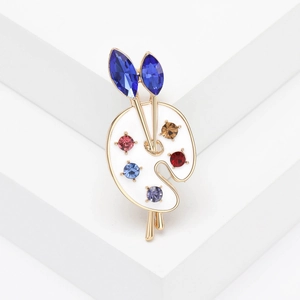 Spilla artistica a forma di tavolozza con strass colorati e pennelli su podio bianco