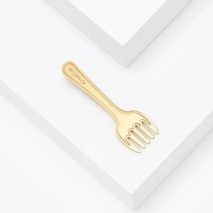Detail shot of golden fork brooch showing the Creative engraving and polished finish