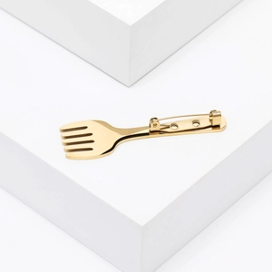 Macro detail of a minimalist golden stainless steel fork brooch with a polished mirror finish