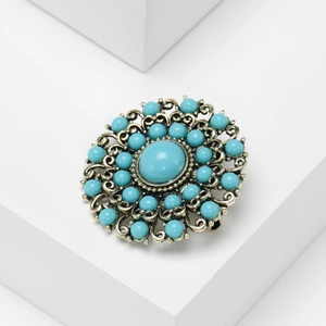 Vintage Baroque turquoise brooch in gold-finish metal on a white geometric display