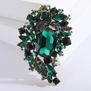 Vintage gold alloy brooch with emerald green crystals on white geometric platform