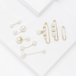 Elegant pearl brooch set with long pins and safety pins on white geometric blocks
