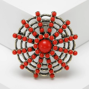 Vintage sunflower brooch with red resin beads and retro metal frame on white geometric blocks
