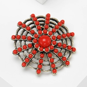Vintage gold metal round brooch with red beads and rhinestones on a white stand