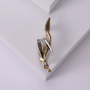 Abstract two-tone flowing metal brooch in gold and silver finish on a white stand