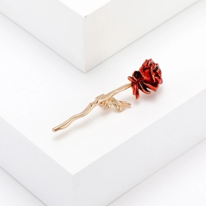 Broche élégante rose rouge en émail avec tige dorée sur présentoir géométrique blanc