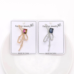 Détail de broches nœuds argent et or avec cristaux sur une carte de présentation