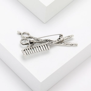 Detail of vintage silver scissor and comb brooch with antique metal texture on white block