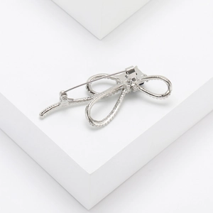 Détail d'une broche nœud argentée ornée de cristaux scintillants sur un fond minimaliste