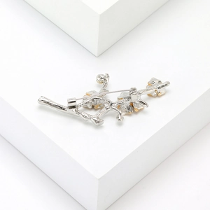Detailed close-up of a silver plum blossom branch brooch with gold petals on white blocks