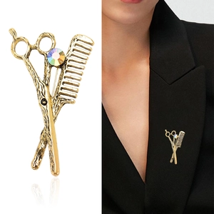 Vintage gold scissors and comb brooch with colorful gemstone on a black suit lapel