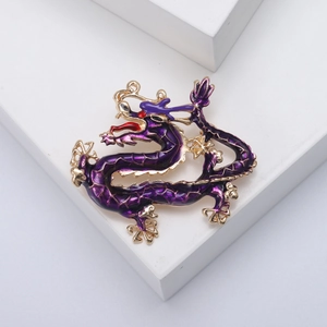 Golden dragon brooch with purple enamel finish and red gemstone eye on white background