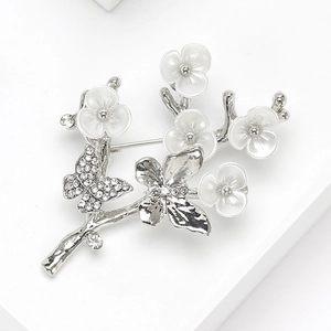 Détails d'une broche papillon argentée avec cristaux étincelants et fleurs blanches