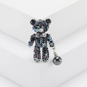 Cute teddy bear brooch with purple and blue crystals on a white geometric platform