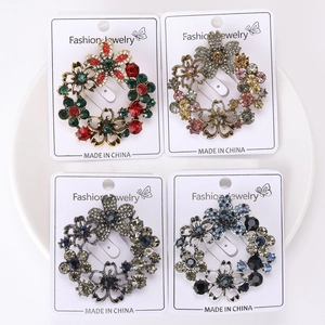 Detailed close-up of four rhinestone flower wreath brooches in multiple colors on a white plate