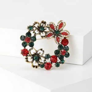 Detailed macro view of vintage gold wreath brooch with vibrant red and green crystals