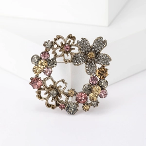 Elegant vintage gold floral wreath brooch with colorful rhinestones on a white pedestal
