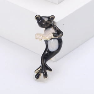 Kreative Emaille-Brosche in Froschform beim Lesen mit schwarzen und cremefarbenen Details