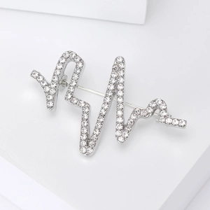 Détail d'une broche ECG argentée avec des strass étincelants sur un piédestal blanc