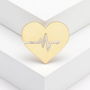 Polished gold heart brooch with minimalist EKG wave on a white geometric display stand