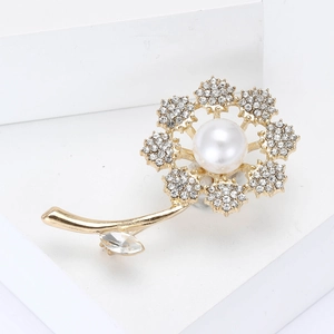 Elegant gold flower brooch with sparkling crystals and large pearl on a white pedestal