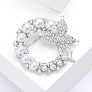 Detailed view of silver wreath brooch with pearls and rhinestone butterfly on a white prop