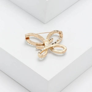 Détail de la broche papillon dorée avec strass sur un support géométrique blanc épuré
