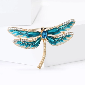 Exquise broche libellule en émail doré avec cristaux bleus sur un piédestal blanc