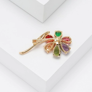 Detail of colorful pear-cut gemstone floral brooch with gold plating on white stone