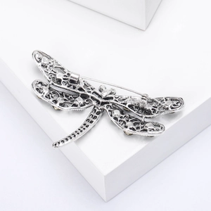 Macro detail of antique silver dragonfly brooch with intricate hollow metalwork and gems