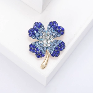 Elegant gold four-leaf clover brooch with gradient blue rhinestones on white platform