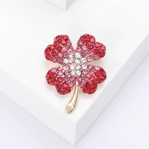 Elegant gold clover brooch with sparkling red and pink rhinestones on a white background