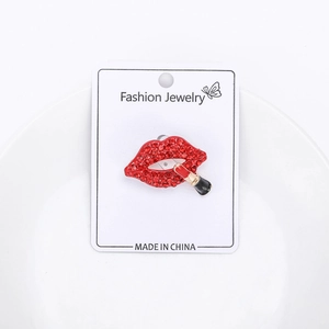 Macro detail of red rhinestone lip brooch with enamel lipstick on white jewelry card