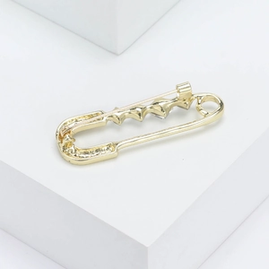 Détail d'une broche dorée avec strass sur des supports géométriques blancs minimalistes