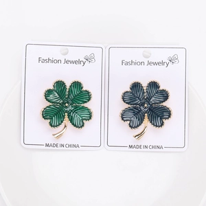 Détail des broches trèfles à quatre feuilles en émail vert et bleu sur carton blanc