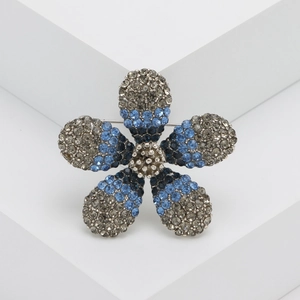 Elegant silver flower brooch with gradient grey and blue rhinestones on a white pedestal