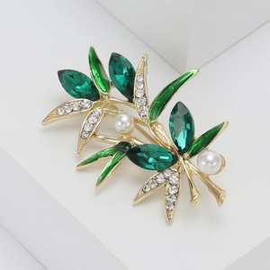 Broche élégante en bambou doré avec cristaux verts et perles sur podium blanc