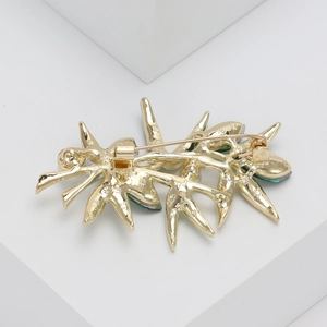 Broche bambou dorée ornée de cristaux verts avec fermoir de sécurité sur fond blanc