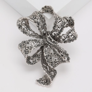 Elegant vintage silver ribbon bow brooch with black rhinestones on a white pedestal