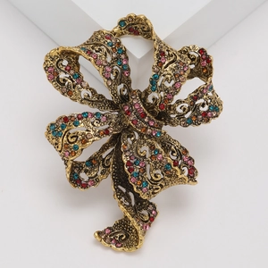 Vintage gold ribbon bow brooch with colorful rhinestones on a white geometric stand